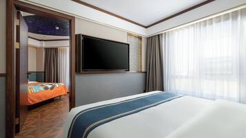 A hotel room with a large bed, a flat-screen TV mounted on the wall, a starry ceiling design, and a view of the outdoors through sheer curtains.