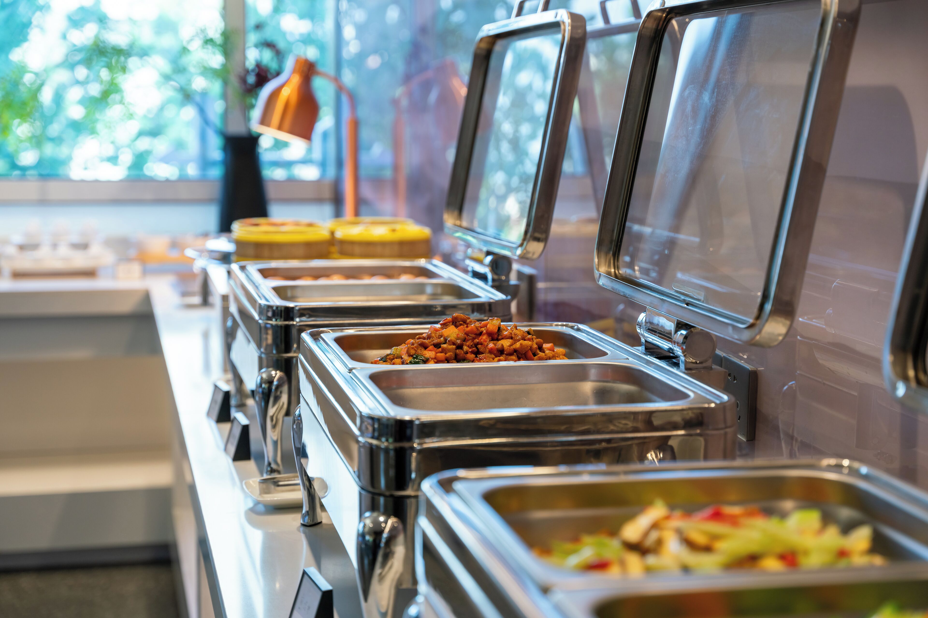 A buffet line with various food options, including a dish with red peppers and a container with a yellow substance.
