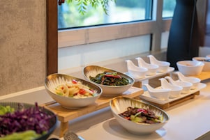 Una mesa de buffet con diversos platos, entre ellos ensaladas y salteados, dispuestos sobre una tabla de madera.