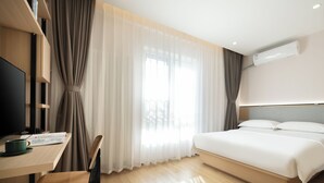 Ein Hotelzimmer mit einem Bett, einem Schreibtisch mit Stuhl, einem Fernseher und einem Fenster mit Vorhängen.