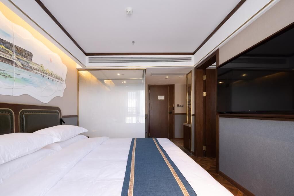 A hotel room with a bed, a painting on the wall, a television, and a door leading to a bathroom.