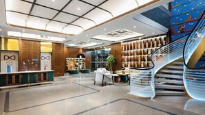 Eine moderne Hotelhalle mit einer zentralen Sitzgruppe, einer Treppe und einer Rezeption.