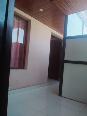 A corridor with a tiled floor, a window with blinds, and a door leading to another room.