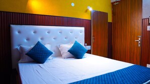 A hotel room with a large bed, two blue pillows, a white comforter, and a wooden wardrobe. - Apna Niwas (Haroli)