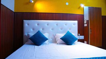 A hotel room with a large bed, two blue pillows, a white headboard, and wooden paneling on the walls.