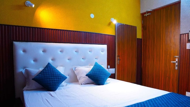 Una habitación de hotel con una cama grande, dos almohadas azules, un edredón blanco y un armario de madera.