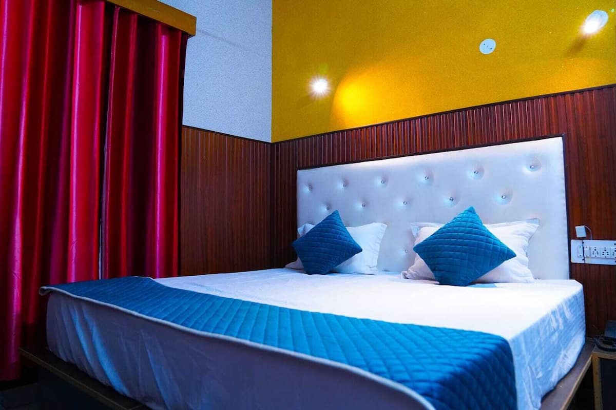 A hotel room with a large bed, red curtains, a white headboard, and a yellow accent wall.