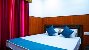 A neatly made bed with blue bedding and pillows, a wooden headboard, and a red curtain to the left. - Apna Niwas (Haroli)