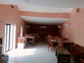 A room with a long table and chairs, a small kitchenette, and a patterned wall. - Apna Niwas (Haroli)