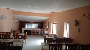 A dining area with multiple tables and chairs, a kitchen area with cabinets and appliances, and a large window providing natural light.