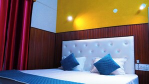 A hotel room with a tufted headboard, a bed with white and blue bedding, and red curtains. - Apna Niwas (Haroli)