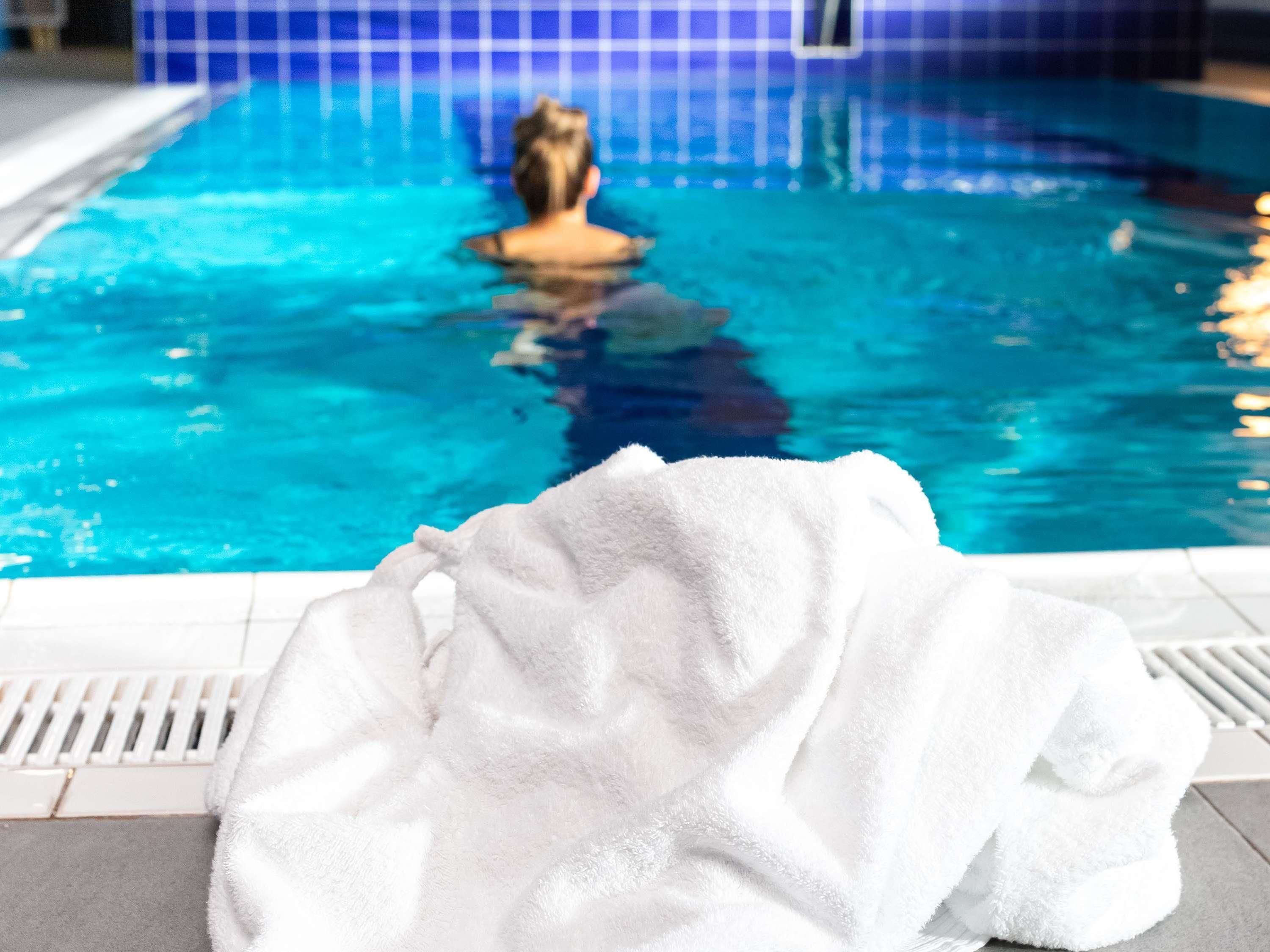 A swimming pool with a person in the water, a white towel on the poolside, and blue tiled walls.
