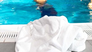 Piscina com uma pessoa na água, uma toalha branca na borda e paredes azulejadas em azul.