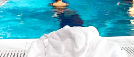 Una piscina con una persona en el agua, una toalla blanca al borde y paredes de azulejos azules.