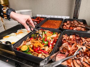 A buffet with various food options including eggs, stir-fried vegetables, and bacon.