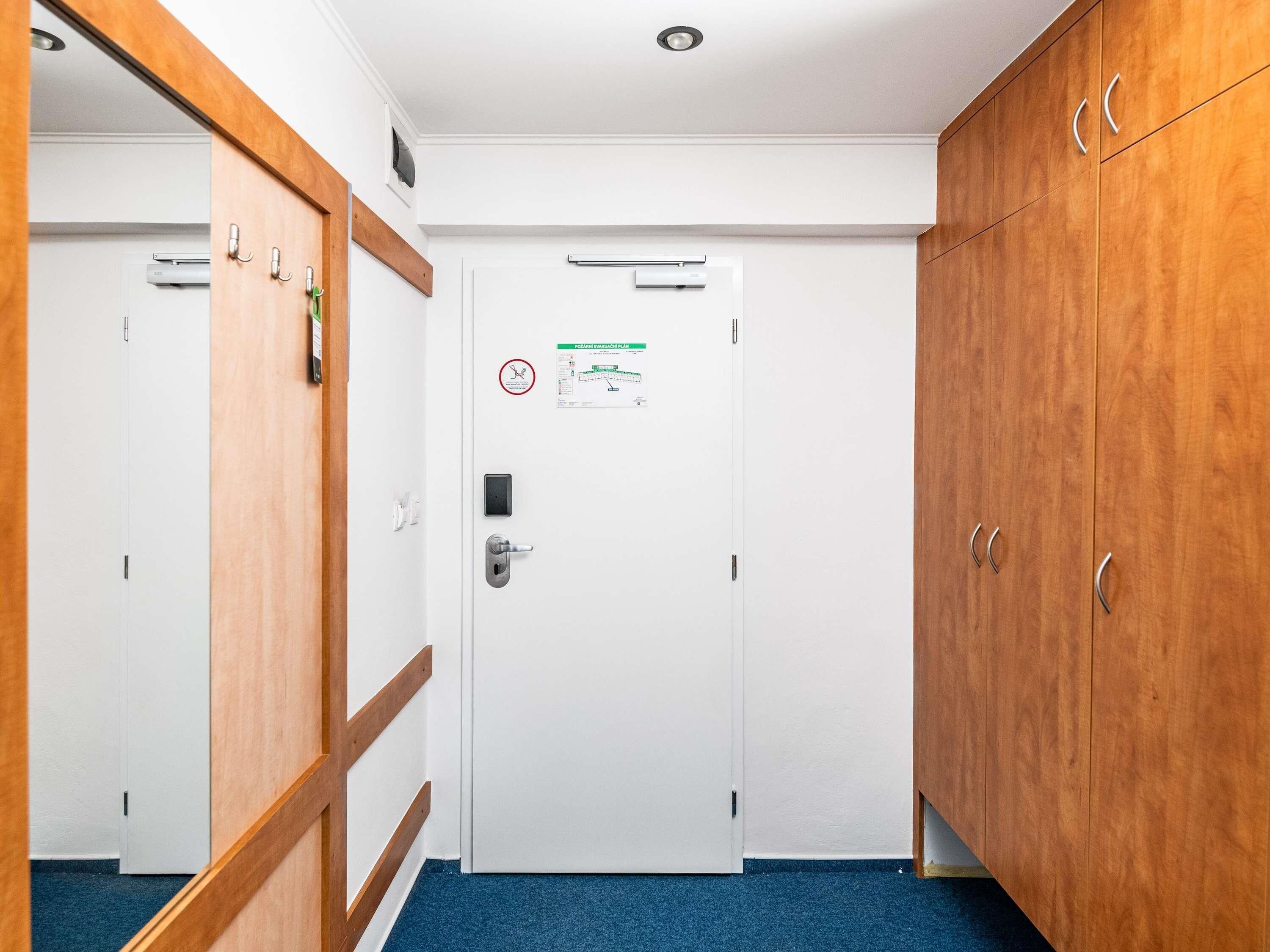 Een gang met een witte deur, een houten garderobe en een blauw tapijt.
