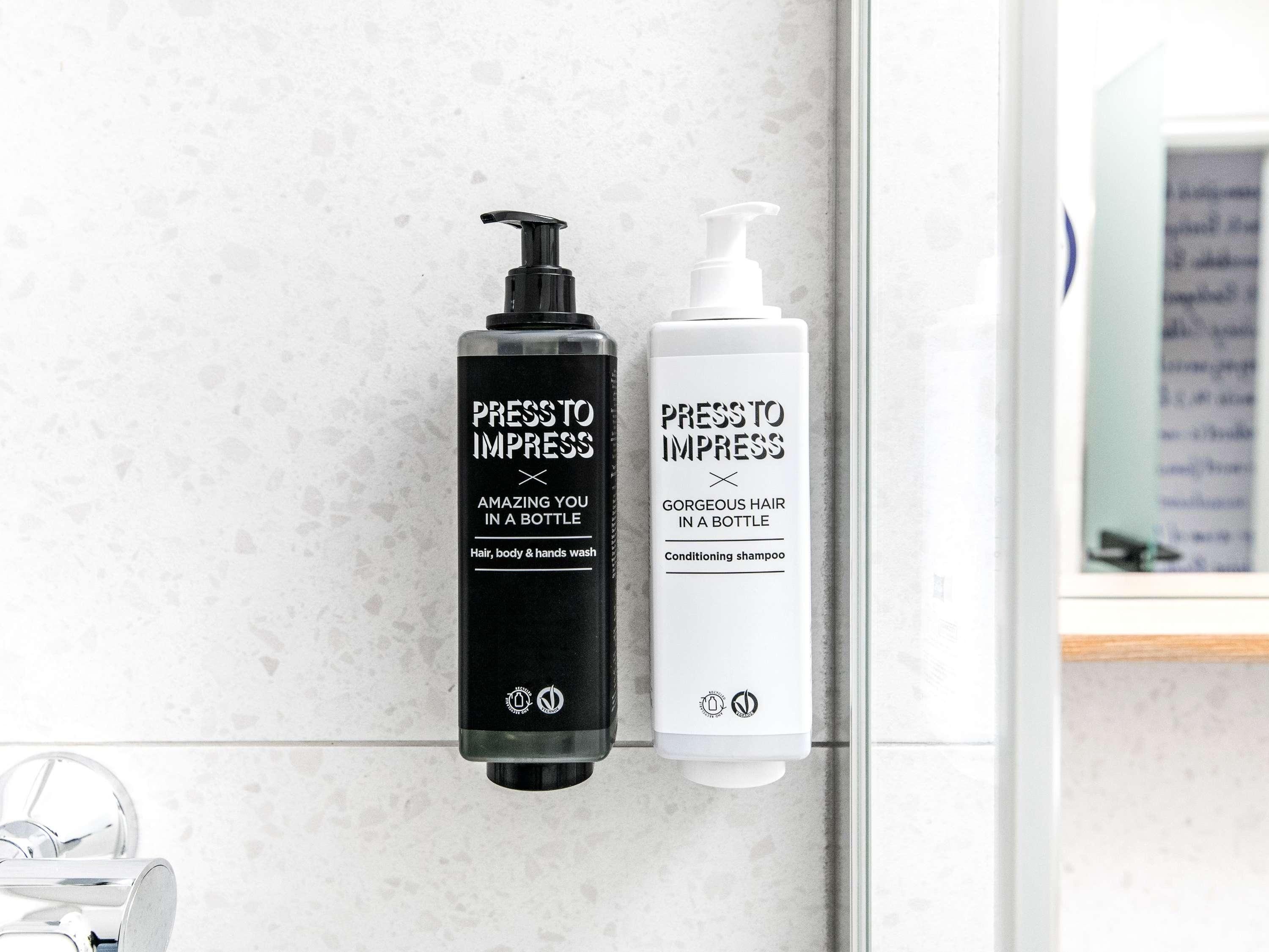 Deux flacons de produits de soins capillaires de la marque « Press to Impress » sont posés sur le comptoir d’une salle de bain.