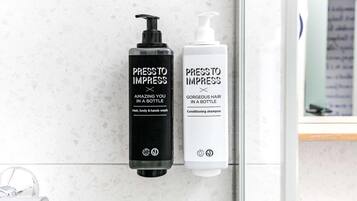 Deux flacons de produits de soins capillaires de la marque « Press to Impress » sont posés sur le comptoir d’une salle de bain.