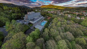 An aerial view of a hotel with multiple floors, a swimming pool, and a parking area surrounded by dense forest. - Ibis Styles Relax Roznov pod Radhostem (Roznov Pod Radhostem)