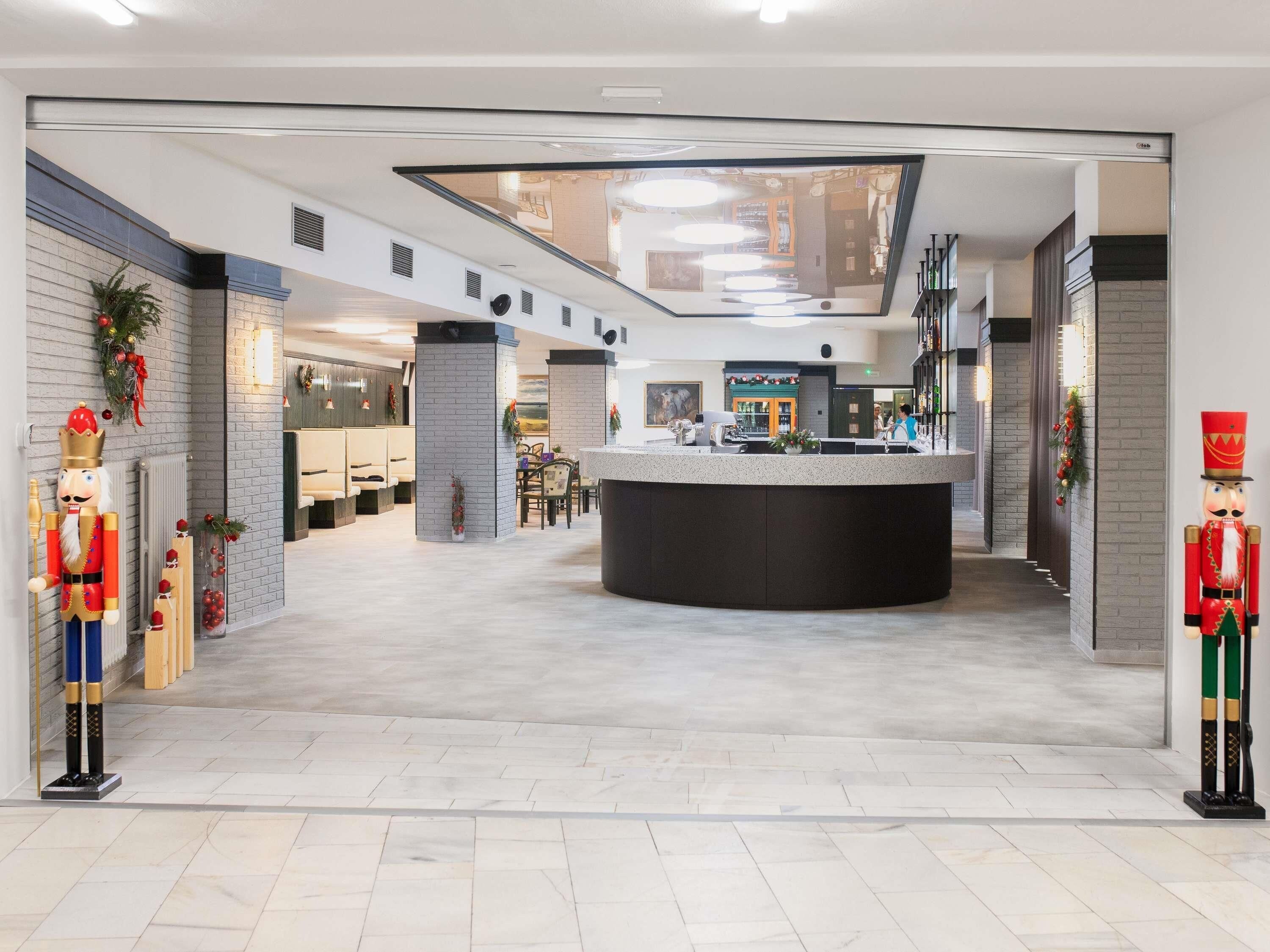 Een moderne hotellobby met een centraal gelegen receptie, zithoeken en uitzicht op de bar en eetruimte.