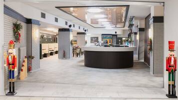 Een moderne hotellobby met een centraal gelegen receptie, zithoeken en uitzicht op de bar en eetruimte.