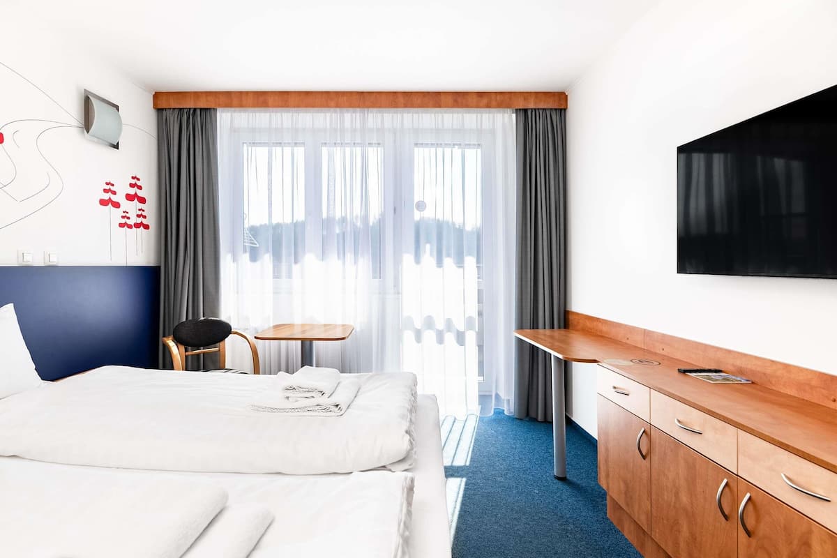 A hotel room with a bed, a desk, a chair, a TV, and a window with curtains.