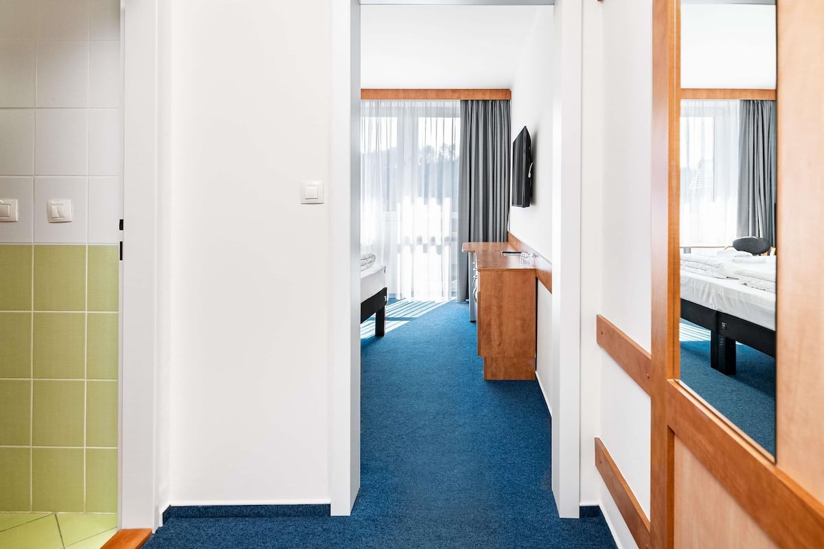 A hotel room with a wooden desk, a bed with a white duvet, and a TV mounted on the wall.