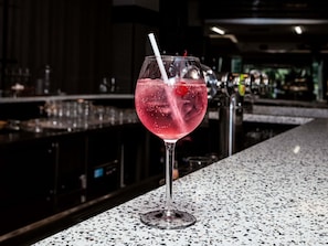 A bar setting with a glass of pink cocktail with ice and a straw, on a speckled countertop.