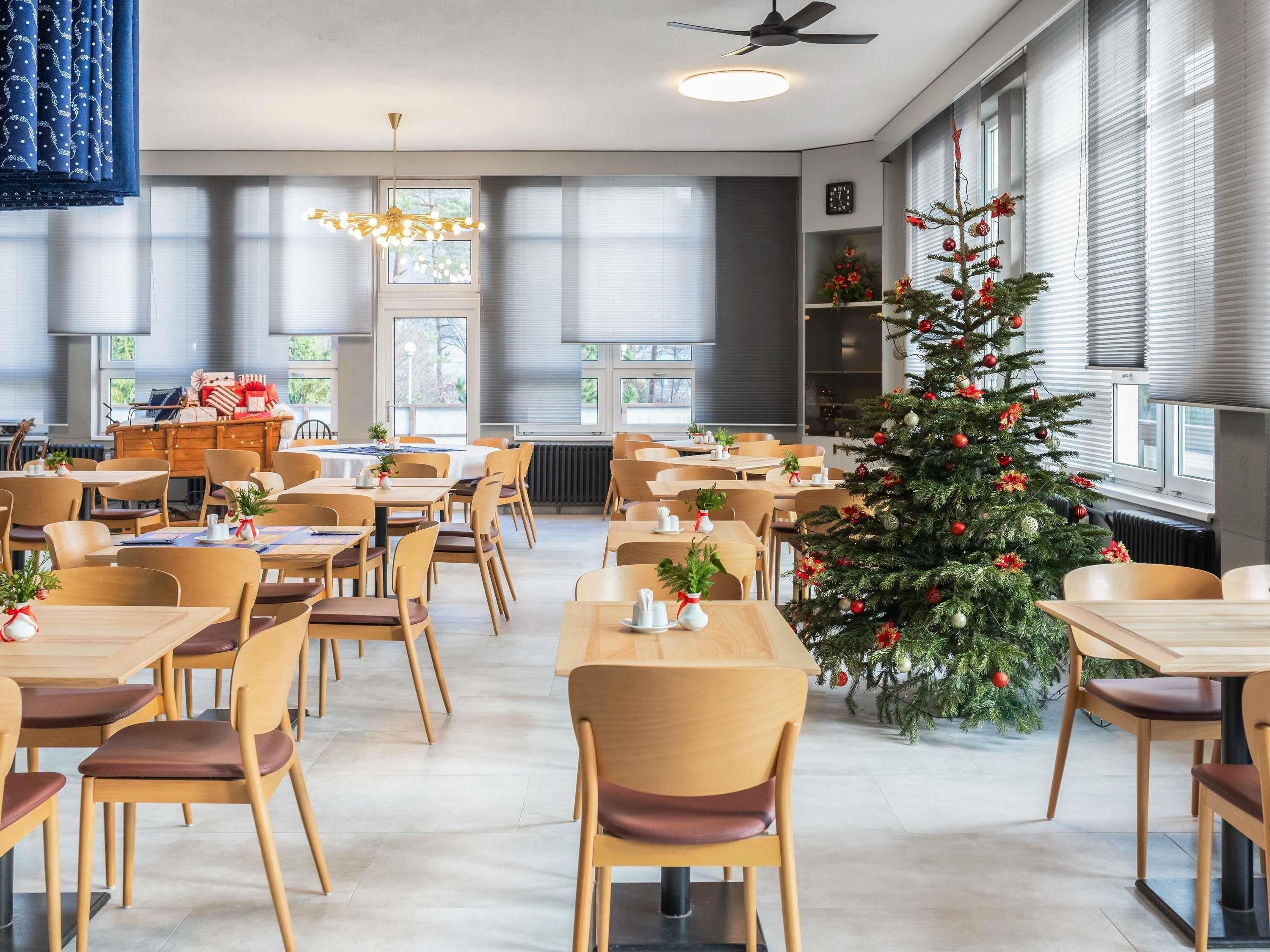 Ein moderner Essbereich mit Holztischen und -stühlen, einem Weihnachtsbaum und Blick durch große Fenster nach draußen.