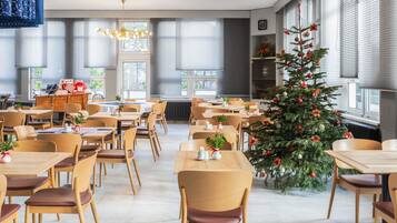 Ein moderner Essbereich mit Holztischen und -stühlen, einem Weihnachtsbaum und Blick durch große Fenster nach draußen.