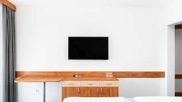 Ein Hotelzimmer mit einem Bett, einem Holztisch, einem an der Wand befestigten Fernseher und einem Kleiderschrank.