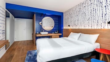 A modern bedroom with a large bed, a round mirror, a wooden nightstand, and a red side table.