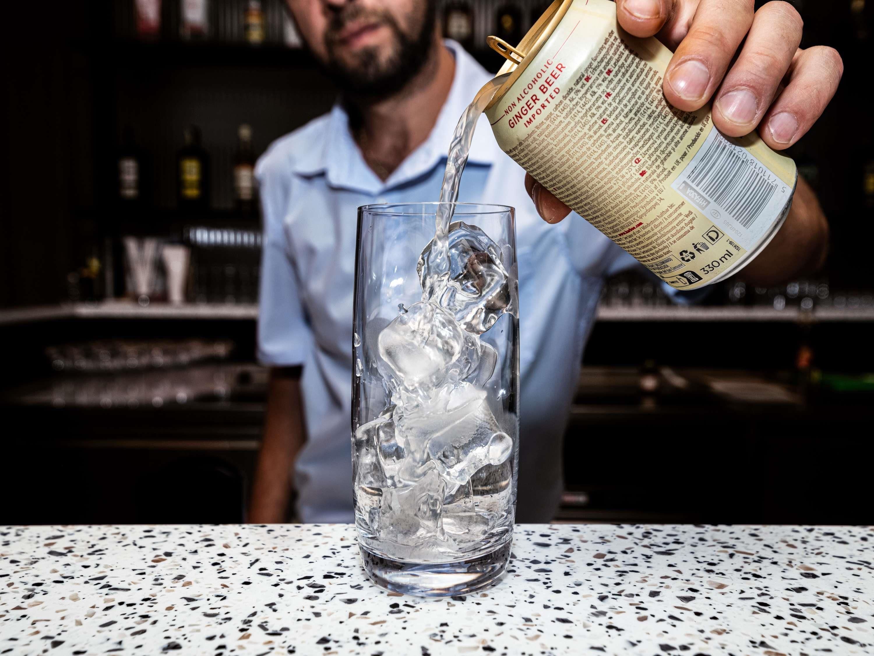 A person pouring a non-alcoholic ginger beer into a glass with ice.