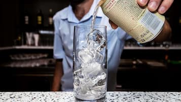 A person pouring a non-alcoholic ginger beer into a glass with ice.