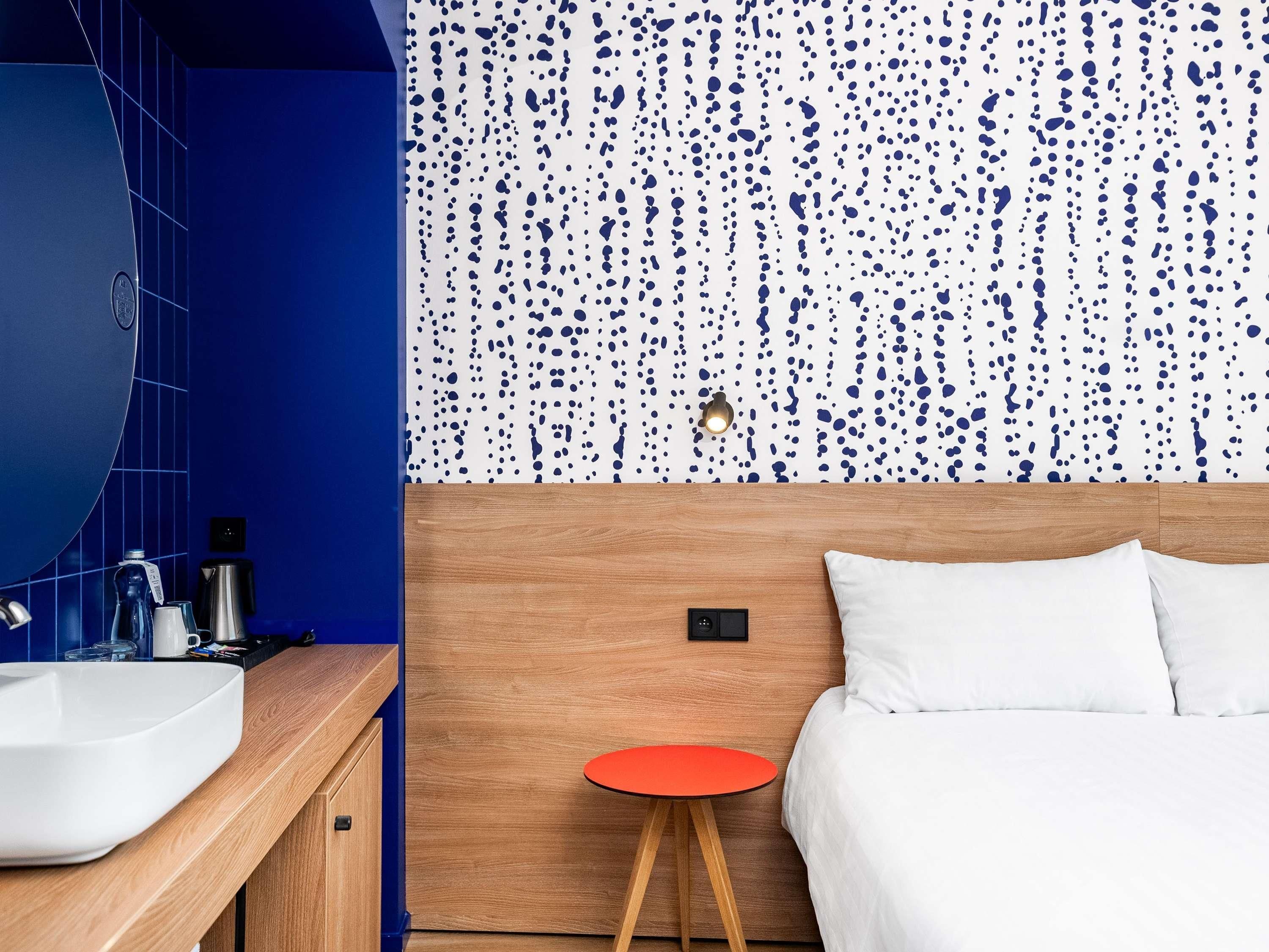 Une salle de bain moderne avec un grand miroir, un lavabo blanc et un mur recouvert de carreaux bleus.