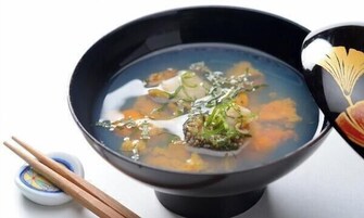 Un tazón de sopa con palillos y un recipiente pequeño de salsa de soja.