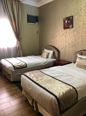 Two single beds with headboards, a window with curtains, a wall-mounted air conditioning unit, and a small picture frame. - Al Wouroud Serviced Appartment (Khamis Mushait)