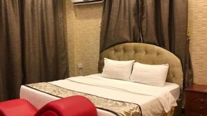 A hotel room with a bed, a red chair, an air conditioning unit, and a wooden floor. - Al Wouroud Serviced Appartment (Khamis Mushait)