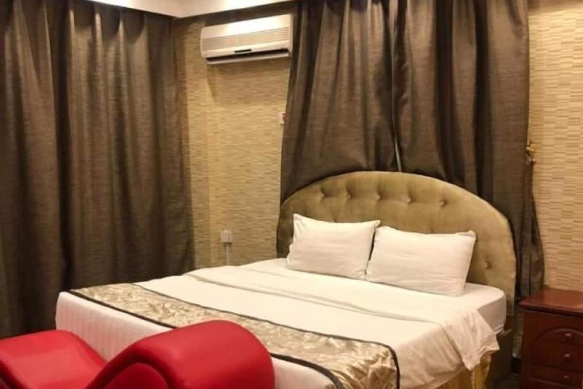 Een hotelkamer met een bed, een rode stoel, een airconditioning en een houten vloer.