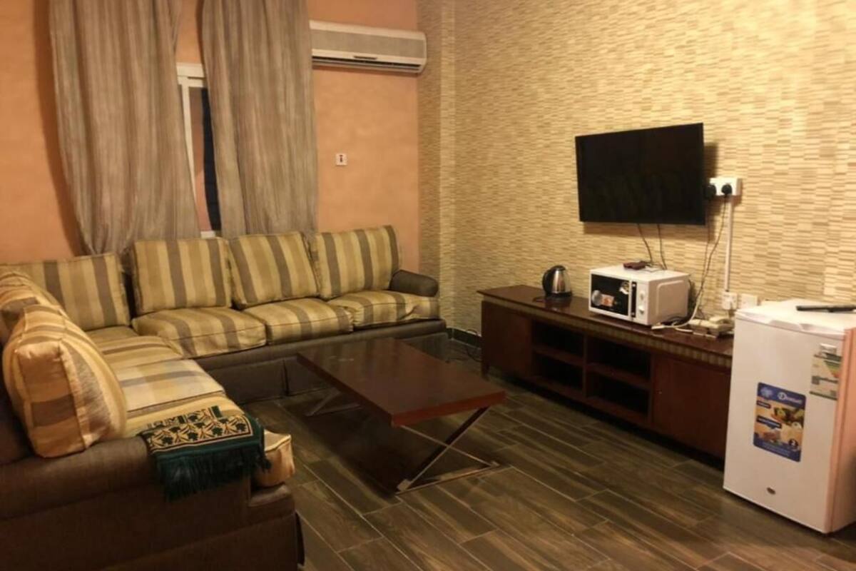 Een woonkamer met een bank, een salontafel, een flatscreen televisie, een magnetron en een koelkast.