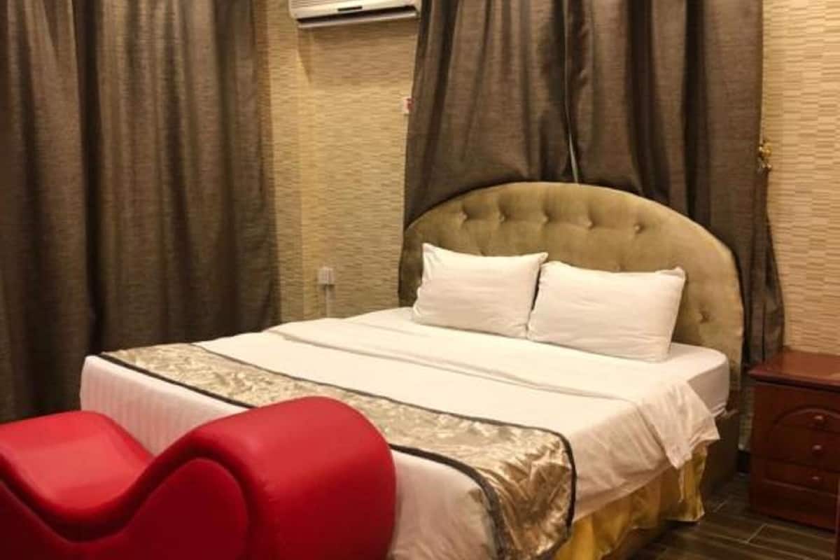 Een slaapkamer met een gestoffeerd hoofdeinde, een bed met witte lakens, een rode bank en een houten vloer.