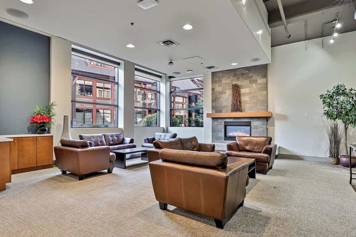 A spacious lobby with leather sofas, a fireplace, large windows, and a view of buildings outside.