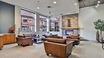 A spacious lobby with leather sofas, a fireplace, large windows, and a view of buildings outside.
