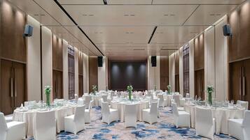 A banquet hall with round tables set for dining, white chairs, and a blue patterned carpet.