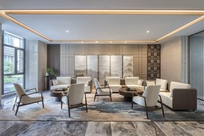 Un salón moderno con un conjunto de sofás, sillones y una mesa de centro. Se aprecia un ventanal grande a la izquierda, un separador decorativo a la derecha y una pared con una pintura de montañas.