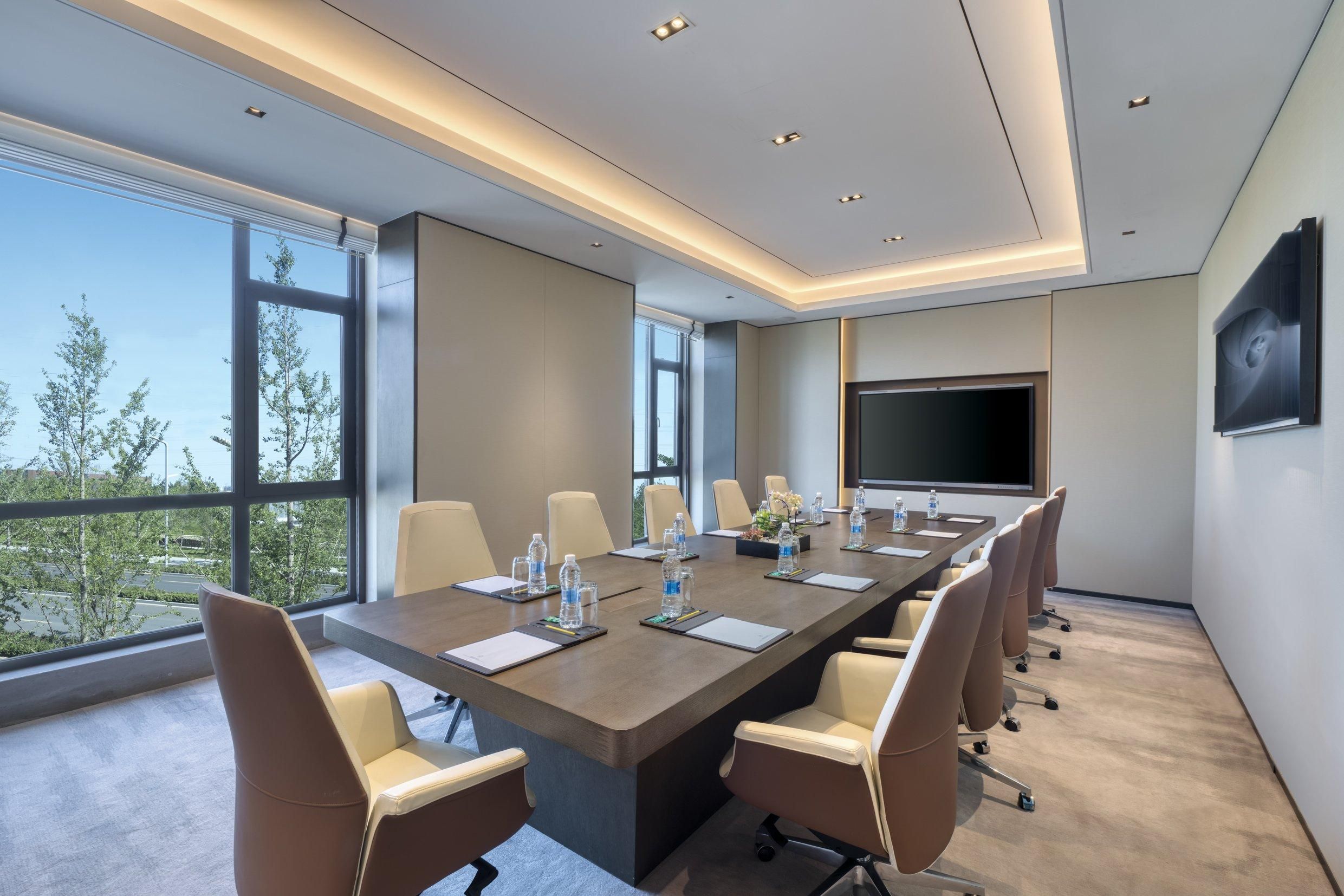 A modern conference room with a long table, beige chairs, and a large screen.