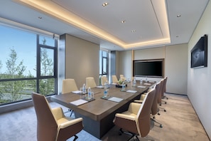 A modern conference room with a long table, beige chairs, and a large screen.
