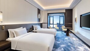Une chambre d’hôtel avec deux lits, un bureau, une chaise et une grande fenêtre donnant sur la ville.