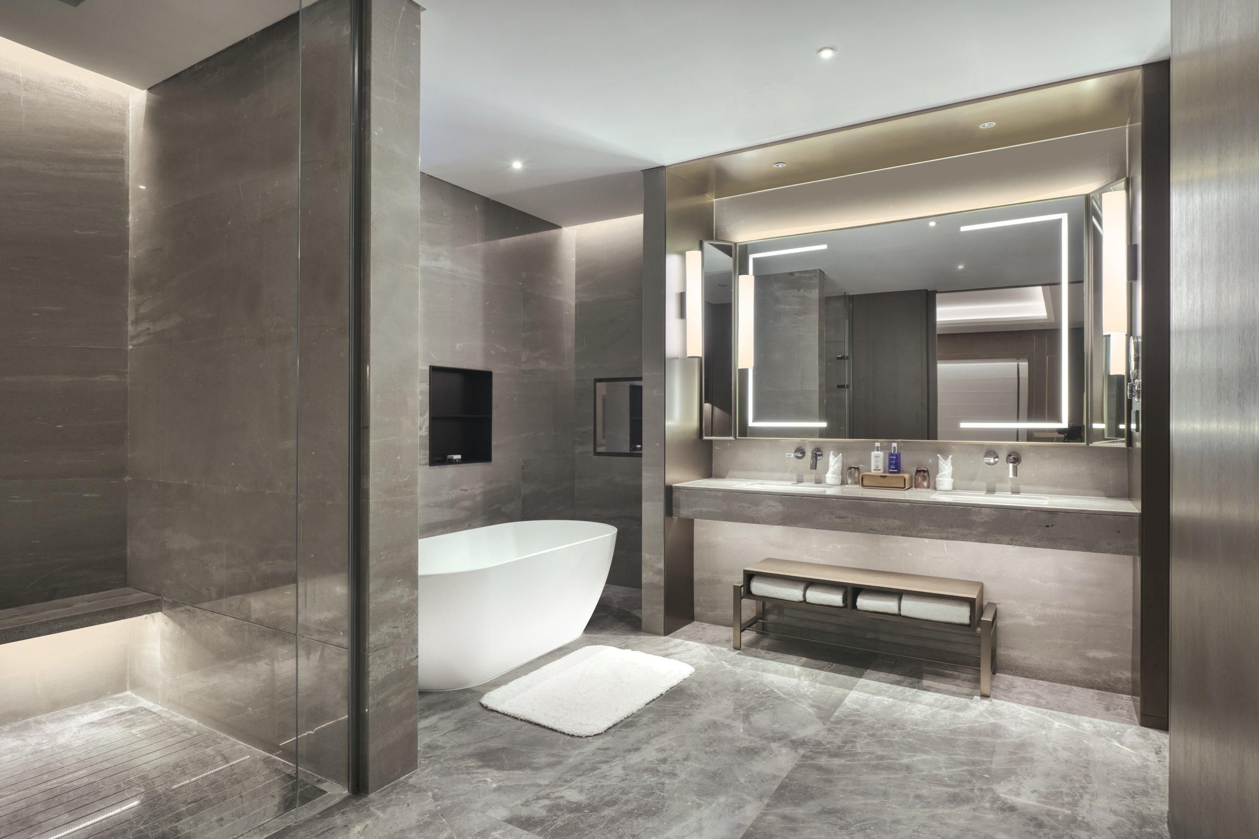 A modern bathroom with a freestanding bathtub, a bench, and a large mirror above the sink.