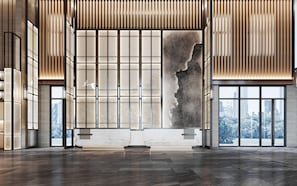 A spacious lobby with a large stone sculpture, wooden paneling, and a view of a cityscape through large windows.